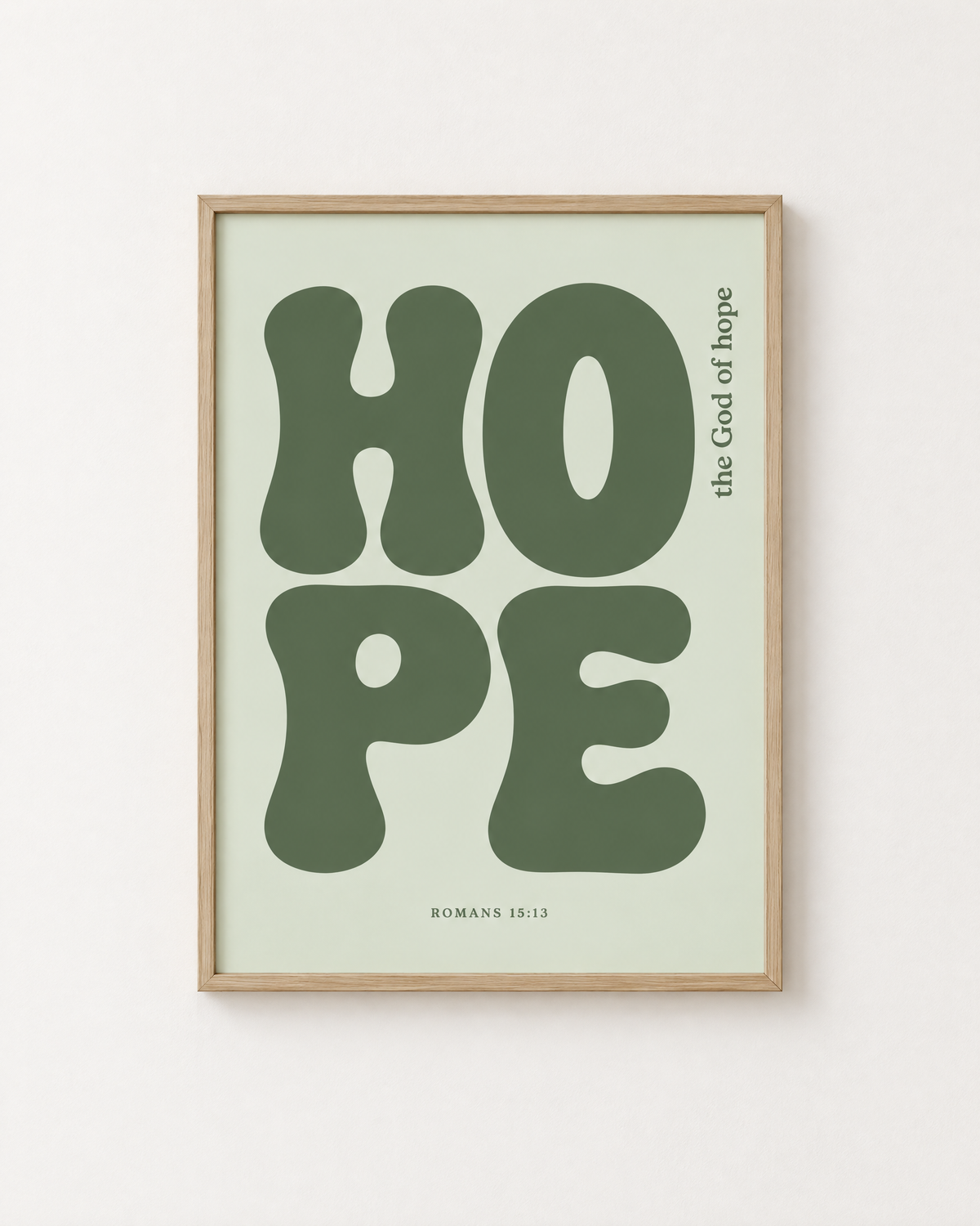 Hope: Sage print in an oak frame on a white wall, reading “The God of hope” (Romans 15:13, KJV). Digital mockup.