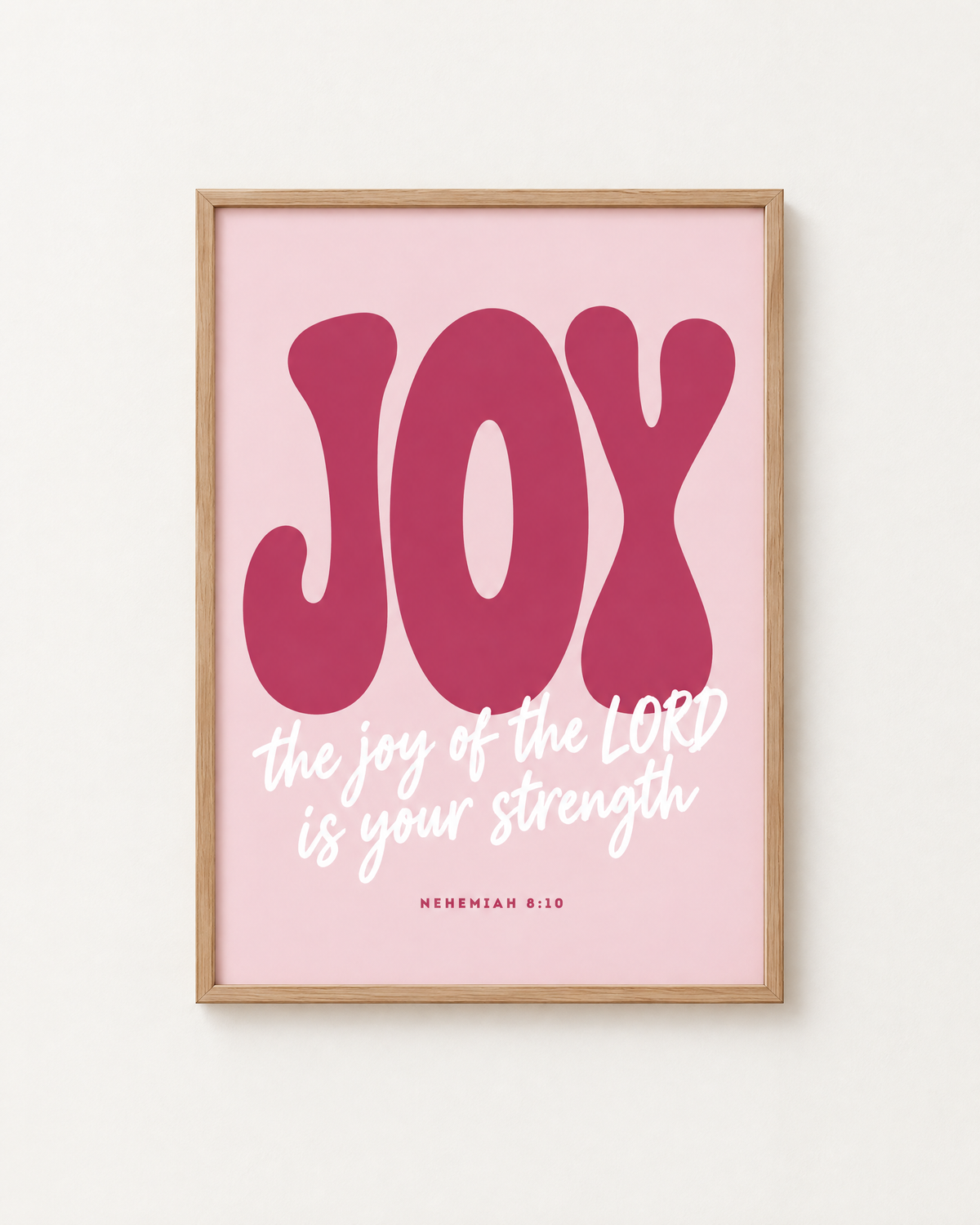 Joy: Blush print in an oak frame on a white wall, reading “The joy of the LORD is your strength” (Nehemiah 8:10, KJV). Digital mockup.