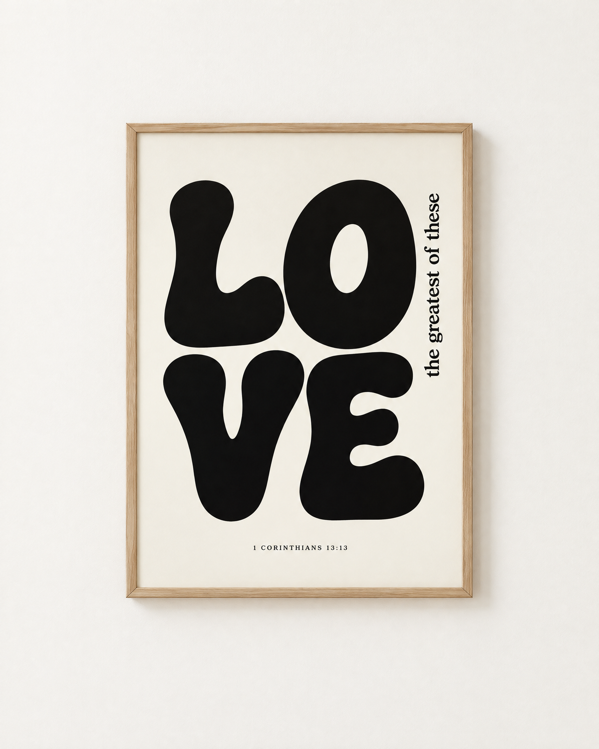 Love: Black & White print in an oak frame on a white wall, reading “the greatest of these” (1 Corinthians 13:13, KJV). Digital mockup.