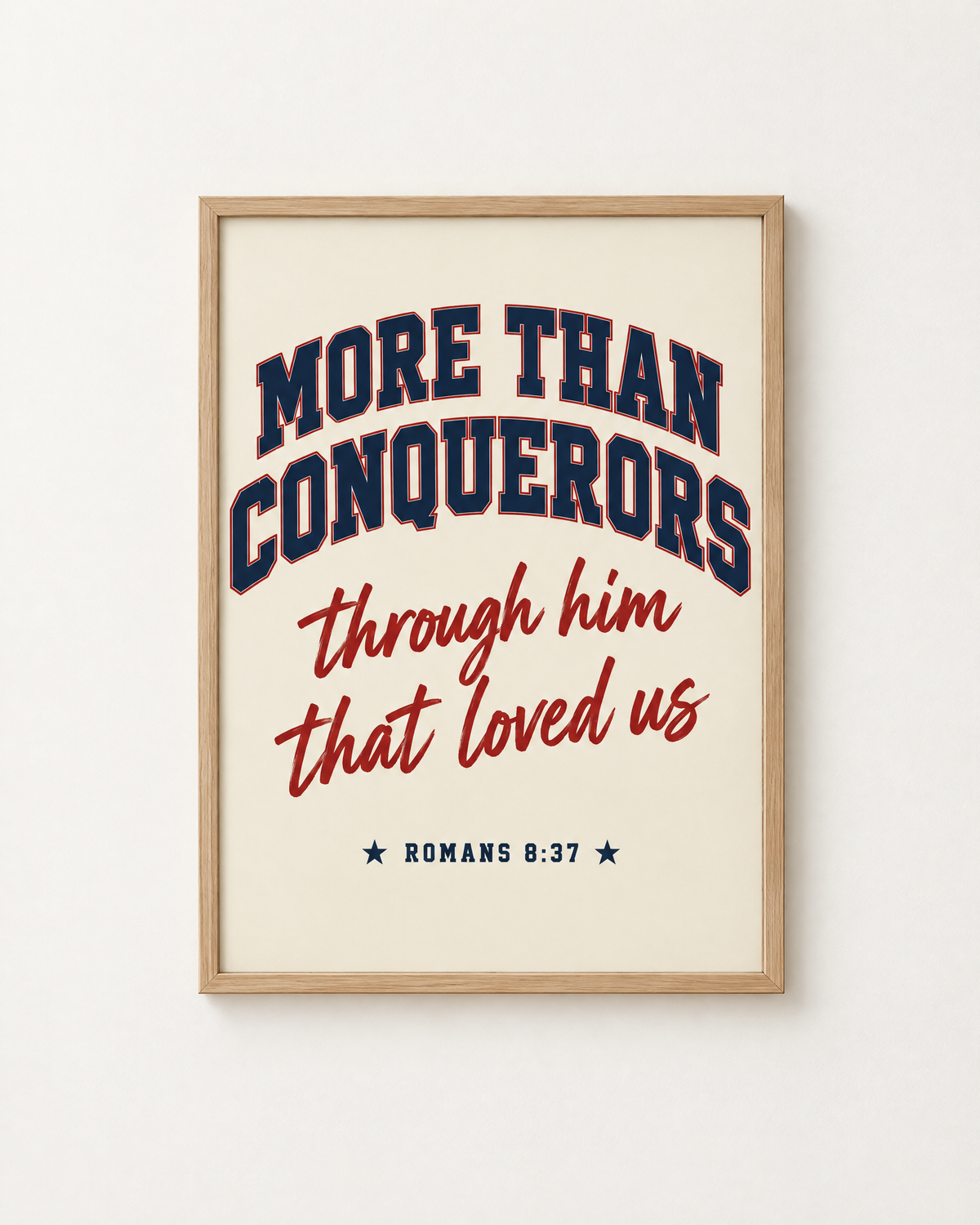 More Than Conquerors: Varsity print in an oak frame on a white wall, reading “More than conquerors through him that loved us” (Romans 8:37, KJV). Digital mockup.