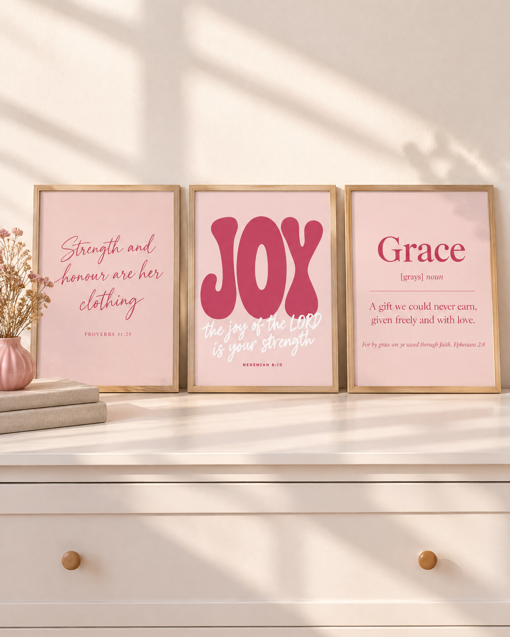 Digital mockup: the Blush Set of 3 in oak frames on a white dresser: “Strength and honour are her clothing” (Proverbs 31:25), JOY “the joy of the LORD is your strength” (Nehemiah 8:10) and Grace (Ephesians 2:8).